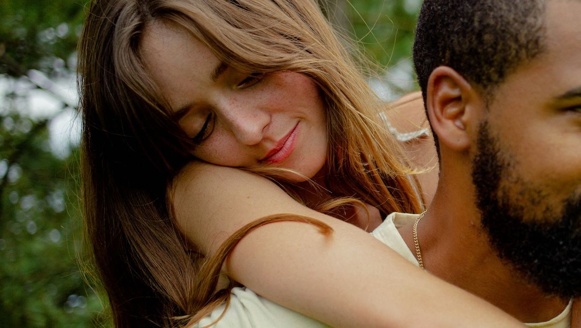 A woman standing behind a man with her arms wrapped around his shoulders