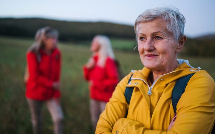 A 60-something woman wearing a yellow raincoat on a hike, looking content and confident