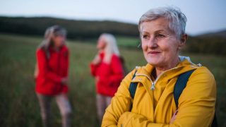 A 60-something woman wearing a yellow raincoat on a hike, looking content and confident