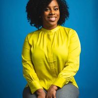 A portrait of Gorgeous West, APC, smiling against a blue studio backdrop.