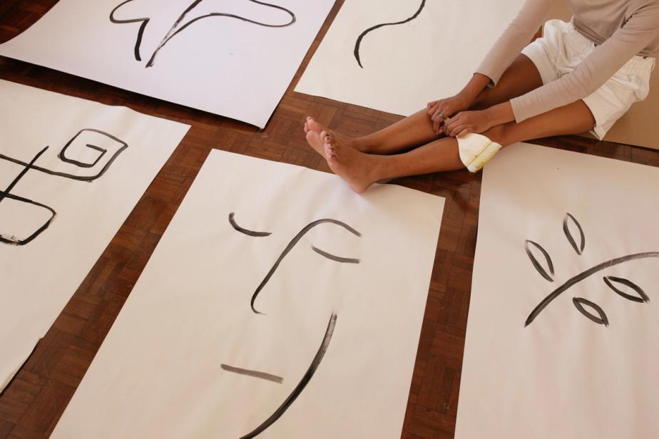 A woman sits on her parquet floor, reflecting on the abstract line art she has painted on posters laid out before her.