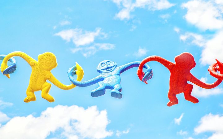 Three different monkey-in-a-barrel figurines, tenuously linked up against the backdrop of a sunny sky, showing the importance of community and a three-pronged approach to fighting stigma.