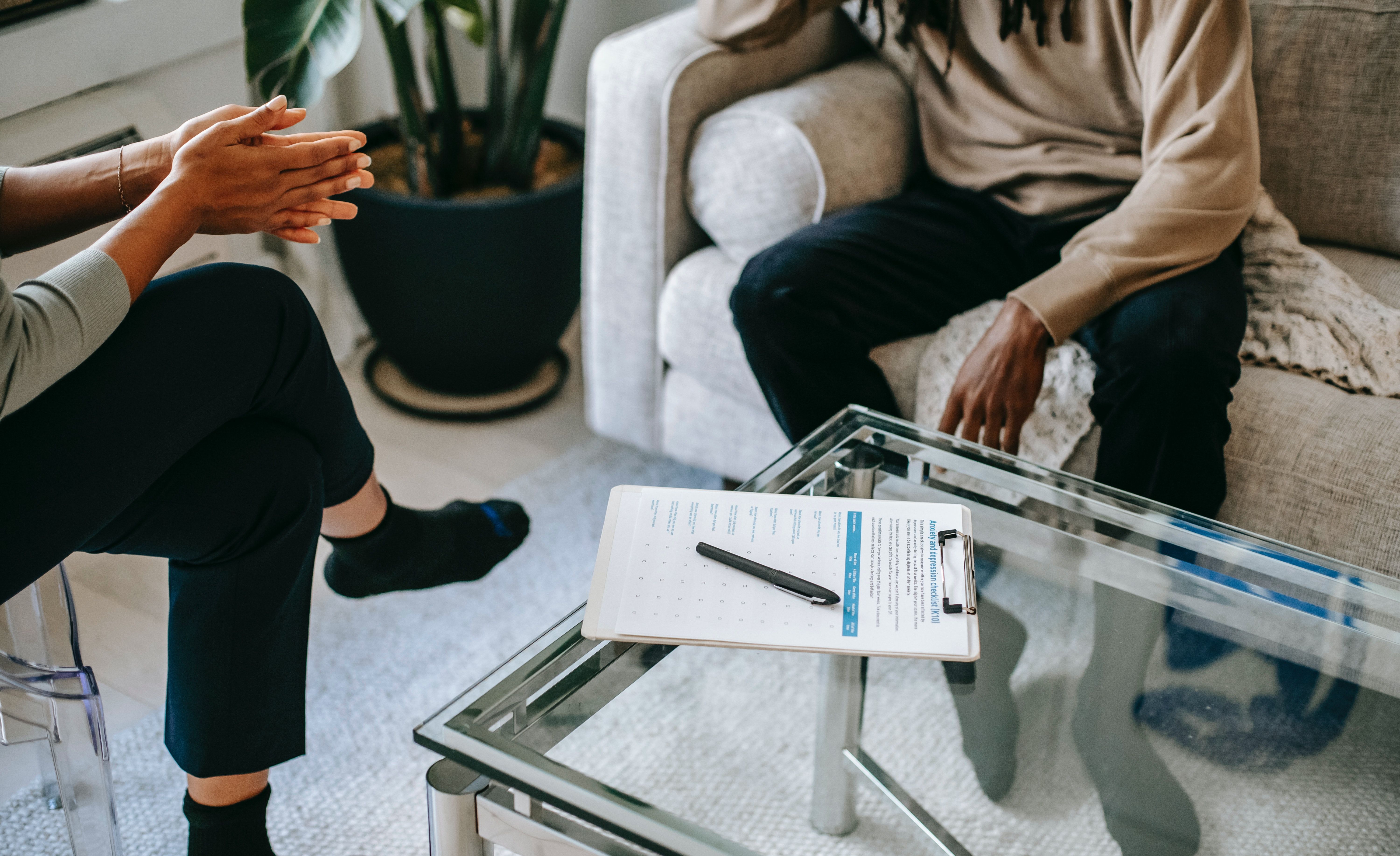 A clipboard with a checklist sits on a coffee table between a therapist and their patient. Perhaps it is a clinical assessment…