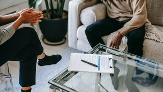 A clipboard with a checklist sits on a coffee table between a therapist and their patient. Perhaps it is a clinical assessment…