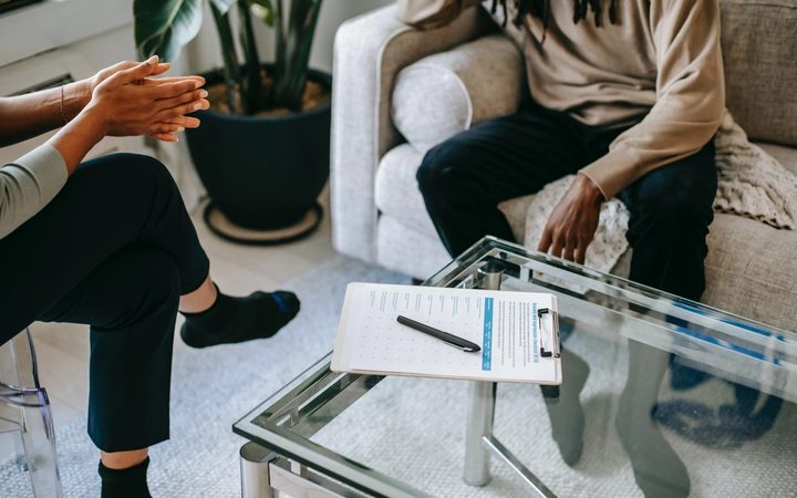 A clipboard with a checklist sits on a coffee table between a therapist and their patient. Perhaps it is a clinical assessment…