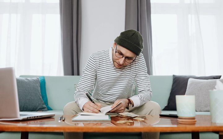 A man works at his coffee table to calculate the cost of therapy after finishing a virtual consultation.