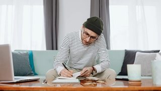 A man works at his coffee table to calculate the cost of therapy after finishing a virtual consultation.
