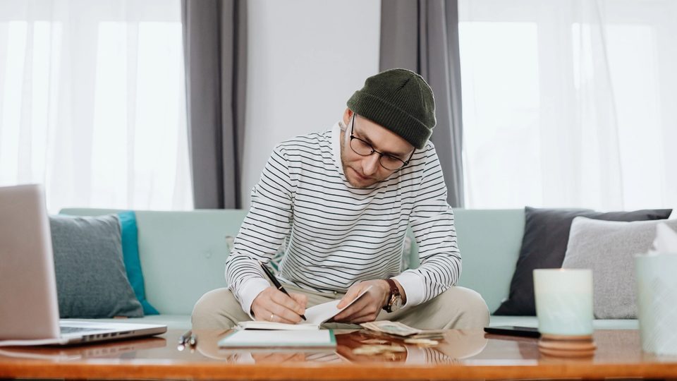 A man works at his coffee table to calculate the cost of therapy after finishing a virtual consultation.