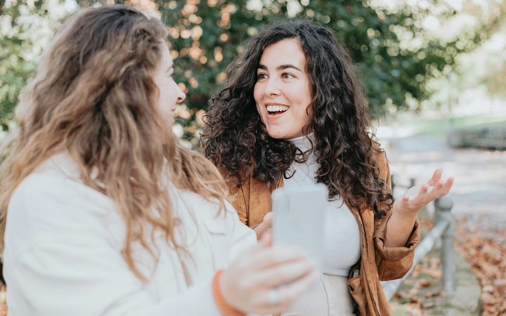Two women sitting in a park, looking surprised by something on their phone