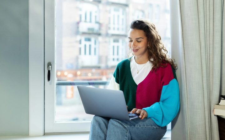 A woman sitting on a window sill using a laptop