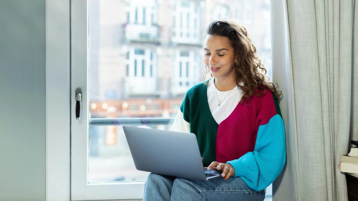 A woman sitting on a window sill using a laptop