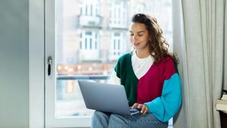 A woman sitting on a window sill using a laptop