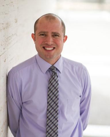 Gary, a sharply dressed therapist in a lilac oxford shirt and tie, smiling to camera in a brightly-lit room.