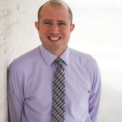 Gary, a sharply dressed therapist in a lilac oxford shirt and tie, smiling to camera in a brightly-lit room.