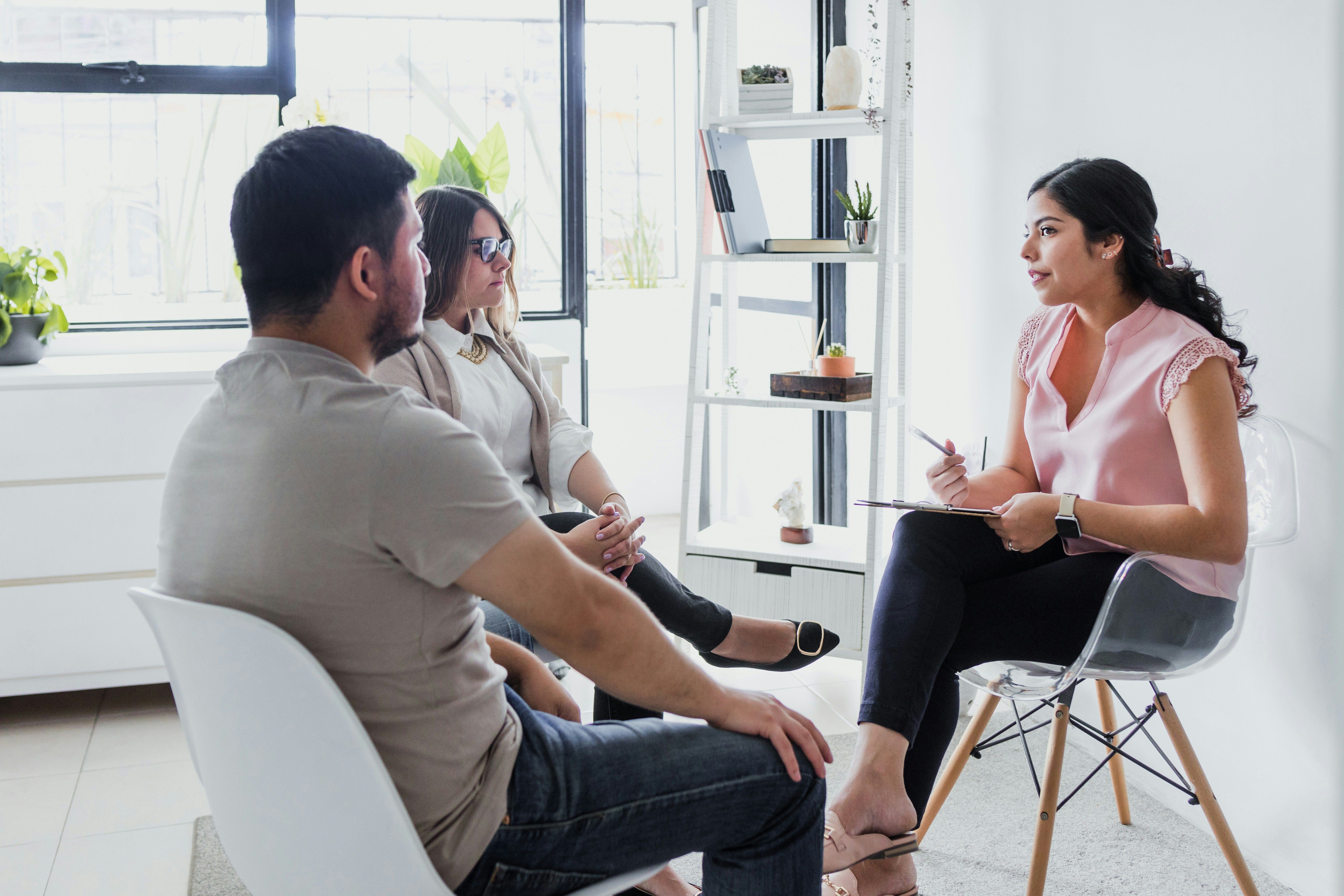 A therapist sits across from a couple during a counseling session in a bright, modern office.