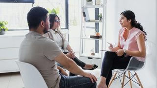 A therapist sits across from a couple during a counseling session in a bright, modern office.