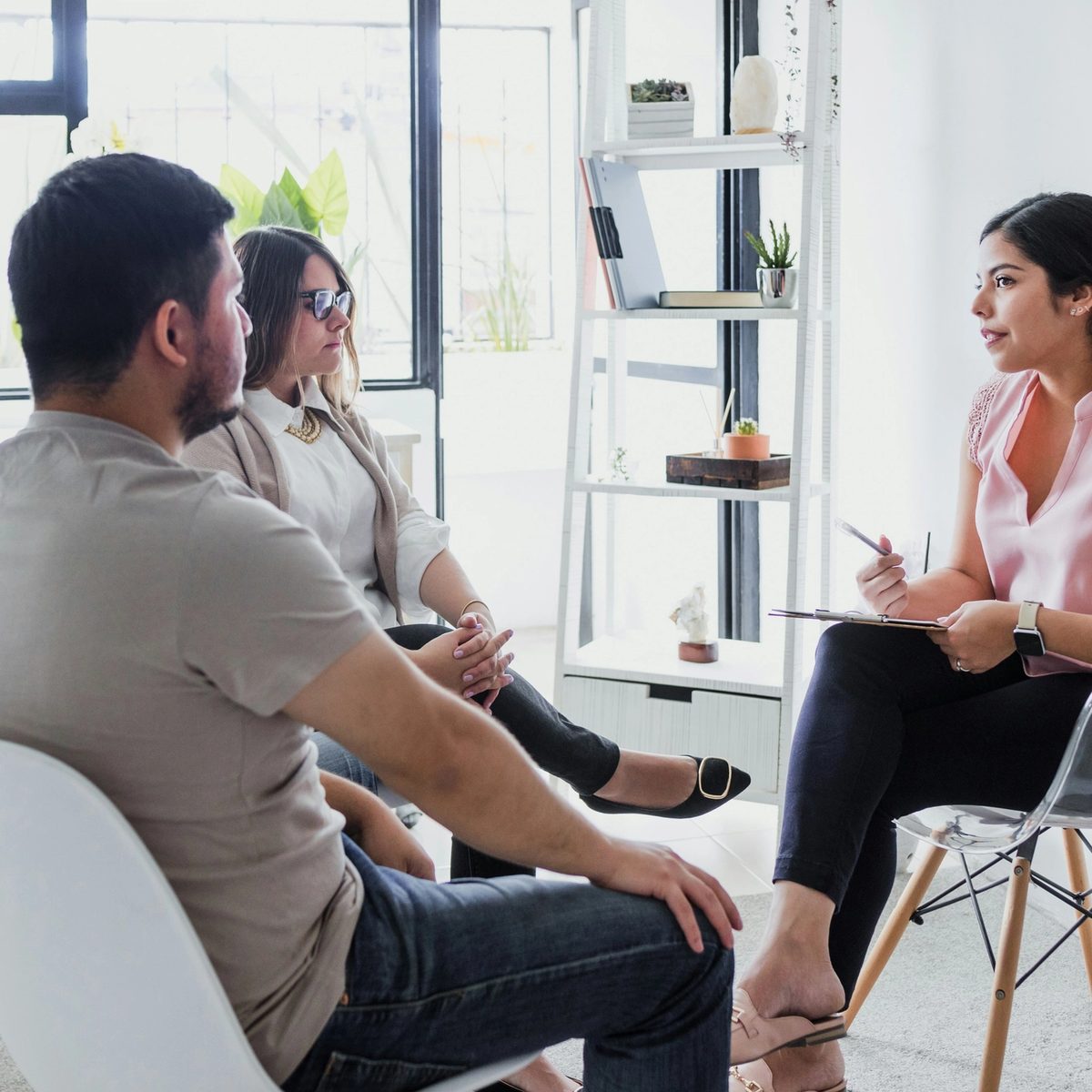 A therapist sits across from a couple during a counseling session in a bright, modern office.