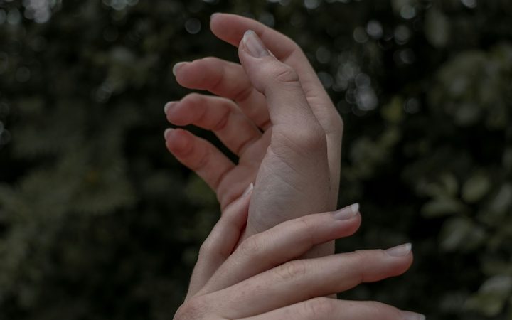 A close up of a person's hand on their wrist in front of a background of green leaves