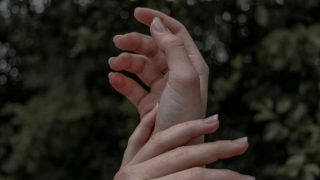 A close up of a person's hand on their wrist in front of a background of green leaves