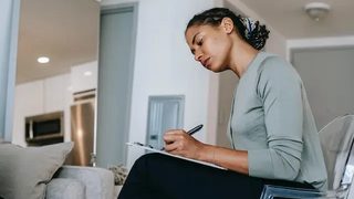A Black therapist taking progress notes on her clipboard while seated in front of a patient.