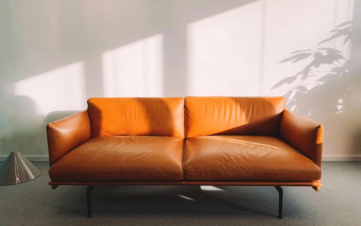 A cognac-colored leather couch, bathed in sunlight shining through the window of a trauma therapist's office.