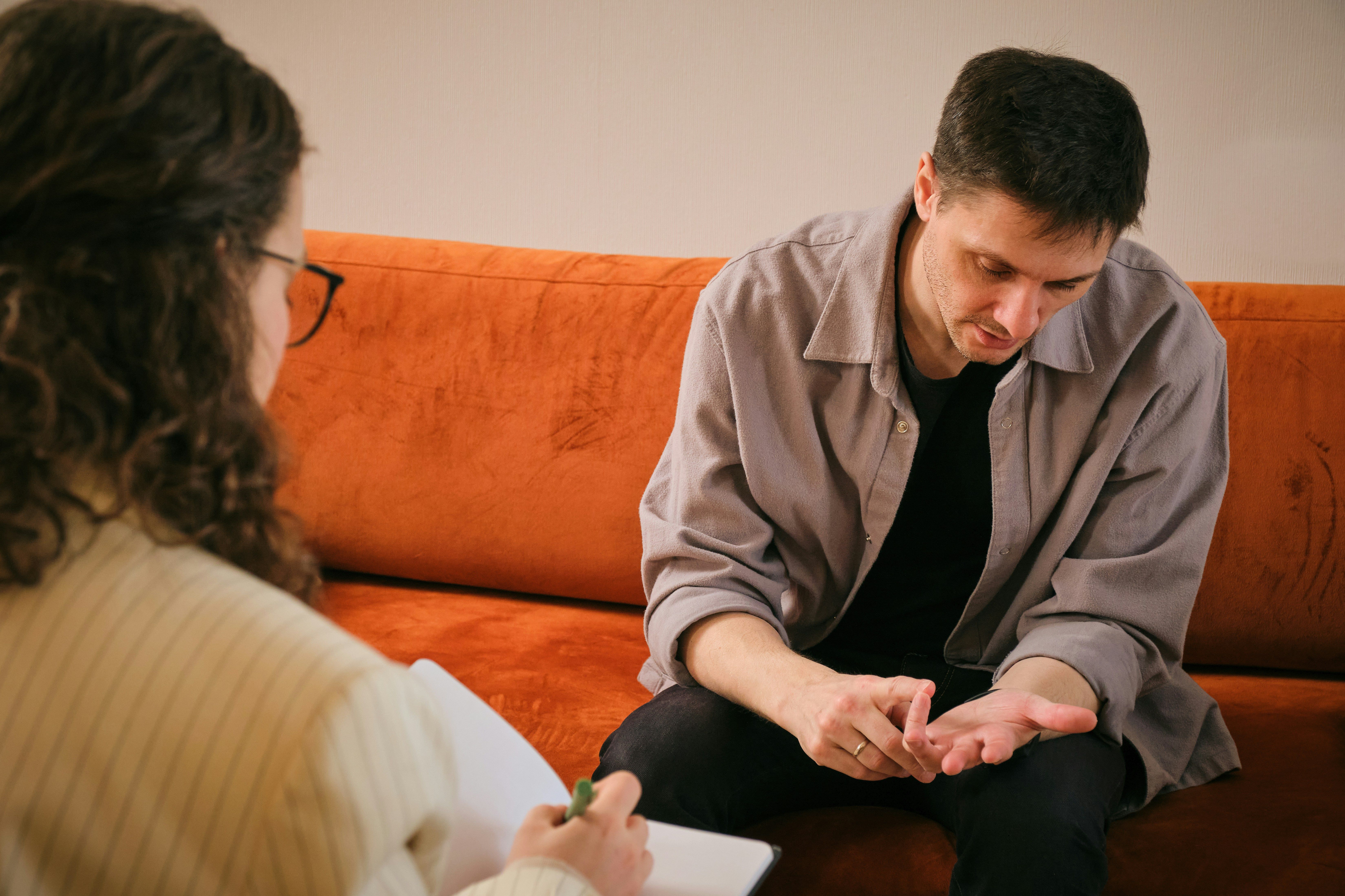 Man sitting on an orange couch speaking with a therapist who is taking notes