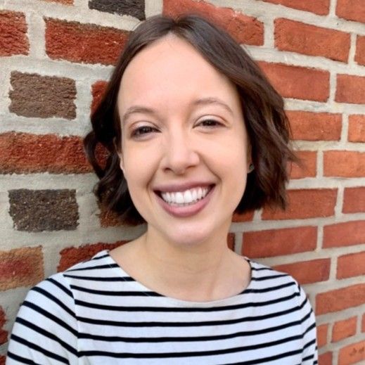 Nancy Ryerson in a striped shirt, standing in front of a brick wall, smiling to the camera.