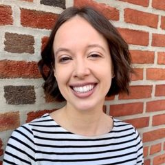 Nancy Ryerson in a striped shirt, standing in front of a brick wall, smiling to the camera.