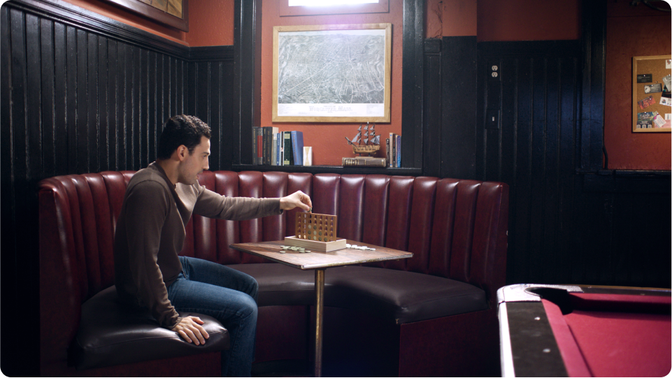 Man in a brown shirt playing connect four in a game room alone