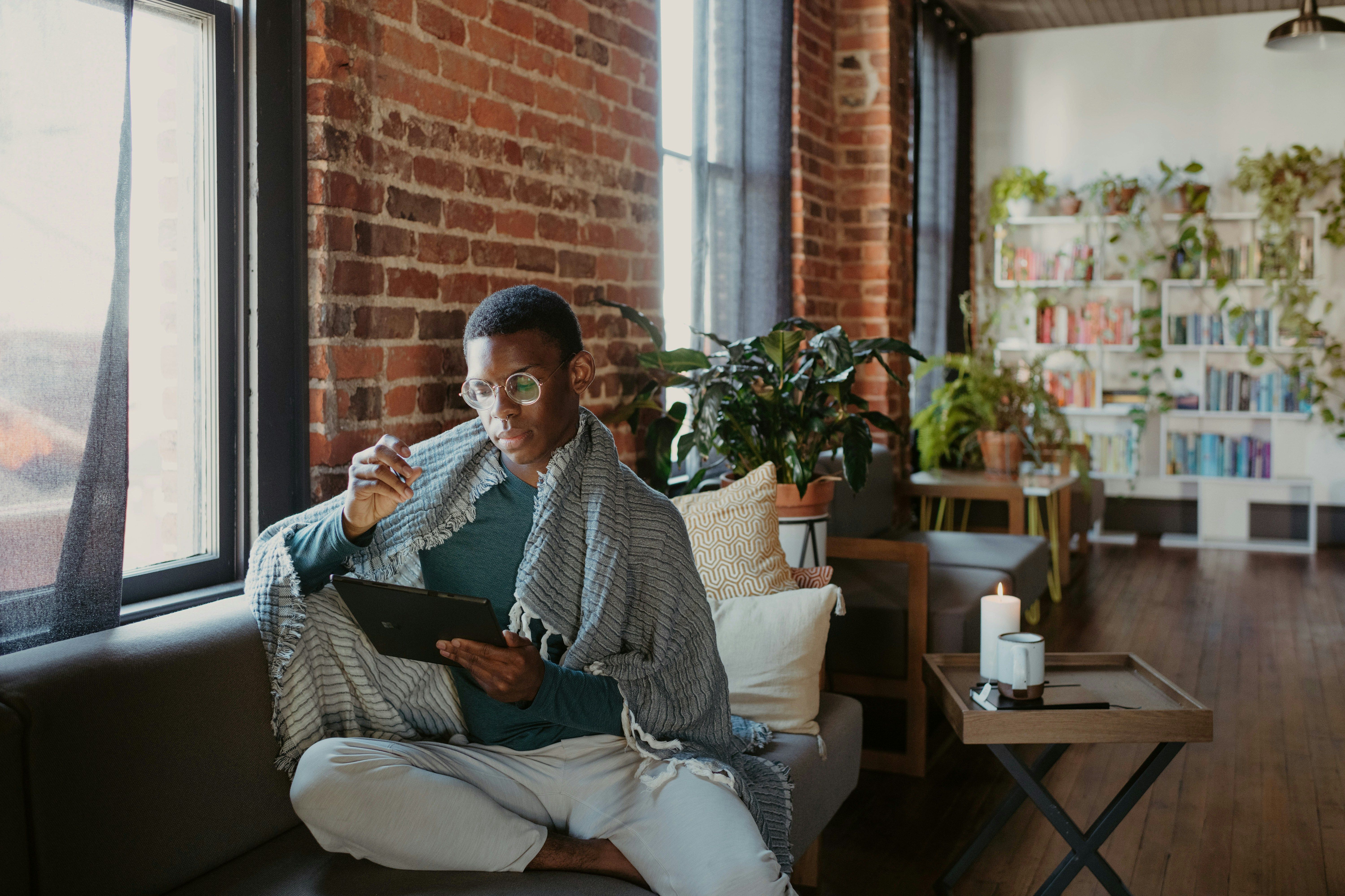 Person with glasses on a couch holding a tablet. 