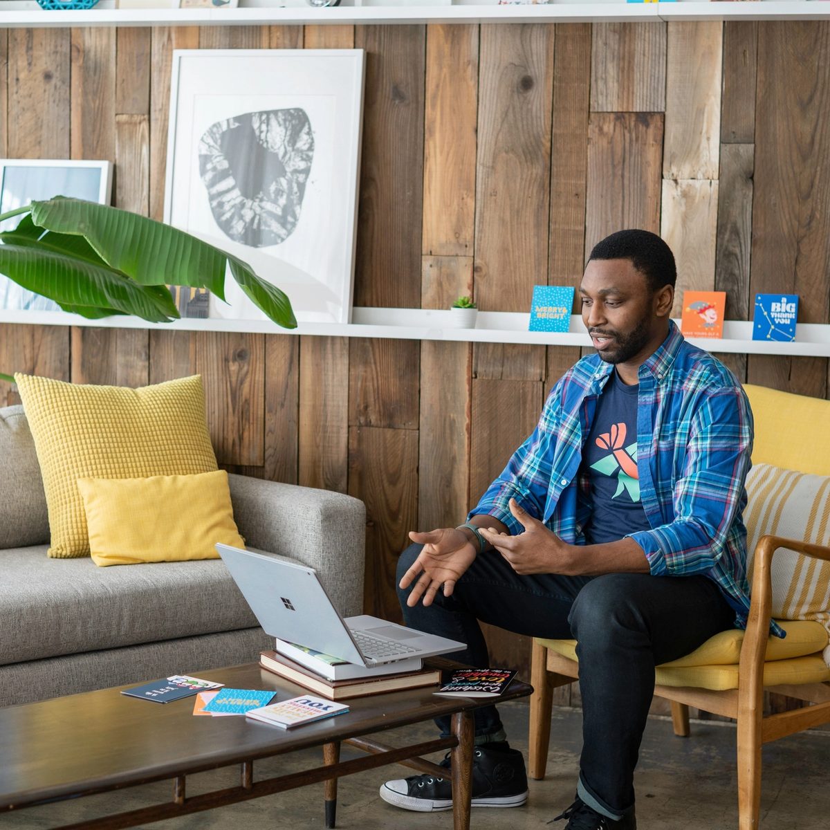 Man in blue and white plaid dress shirt and black pants sitting on couch using macbook