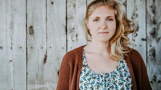An emotionally exhausted therapist steps outside for fresh air, a rugged fence behind her.
