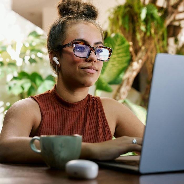 A female therapist is creating AI prompts on her laptop in a sunny, plant-filled office