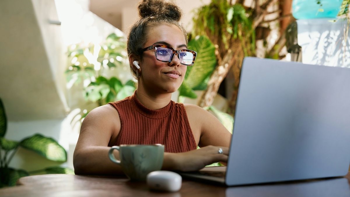 A female therapist is creating AI prompts on her laptop in a sunny, plant-filled office