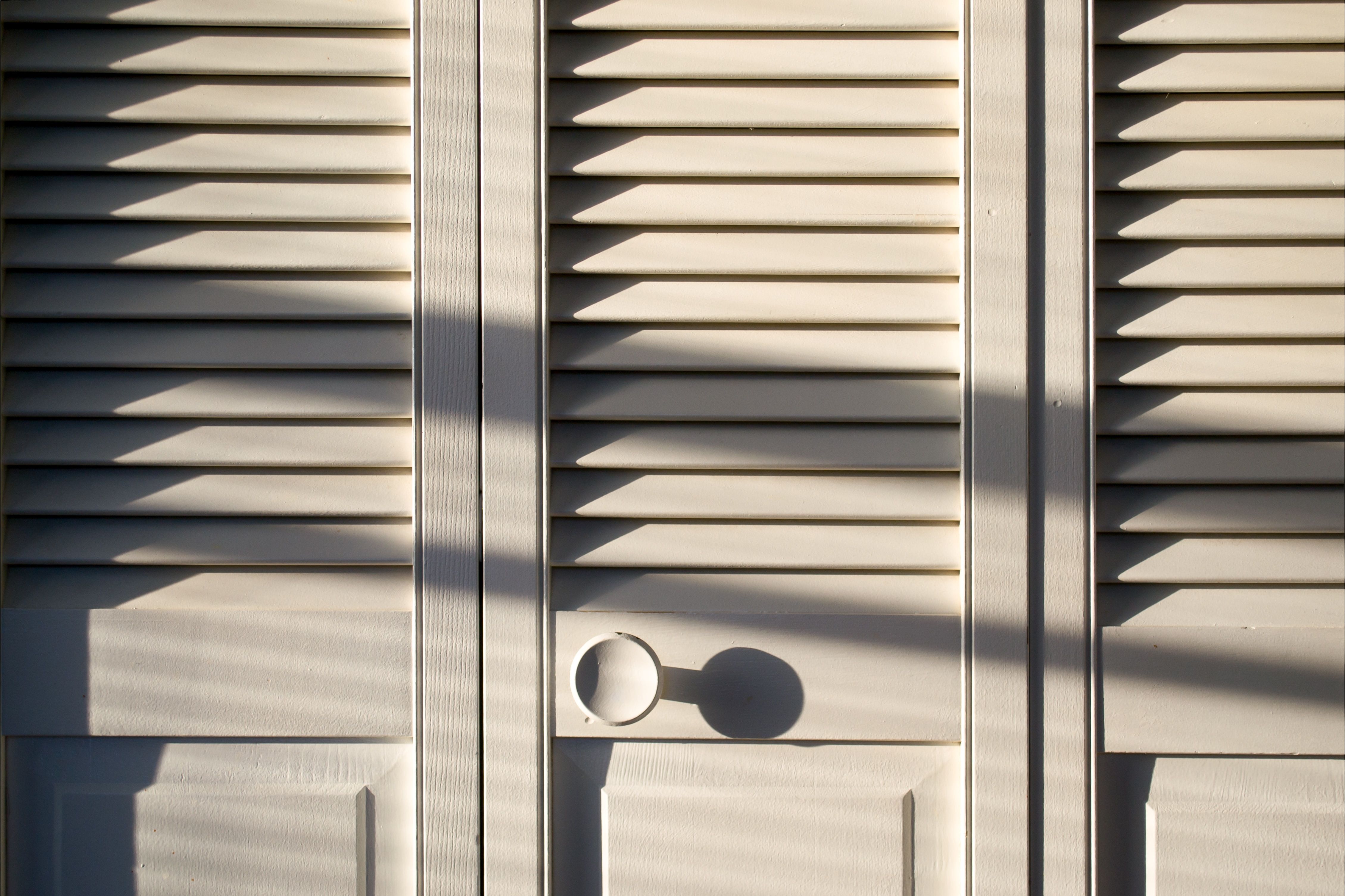Closed closet doors thrown into relief by shadows from bright afternoon sunlight.