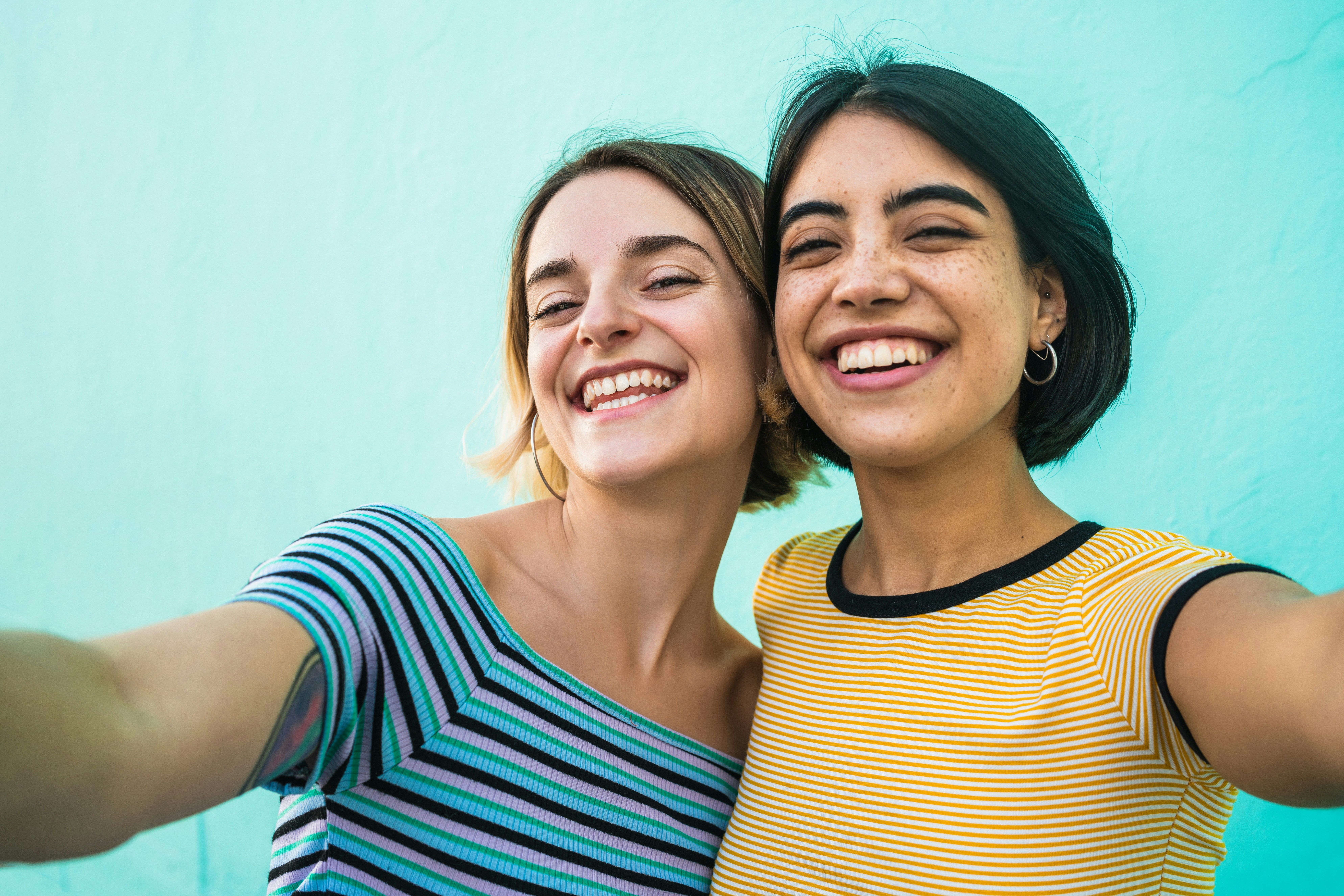 Two women friends wearing t-shirts smiling in front of a blue wall.