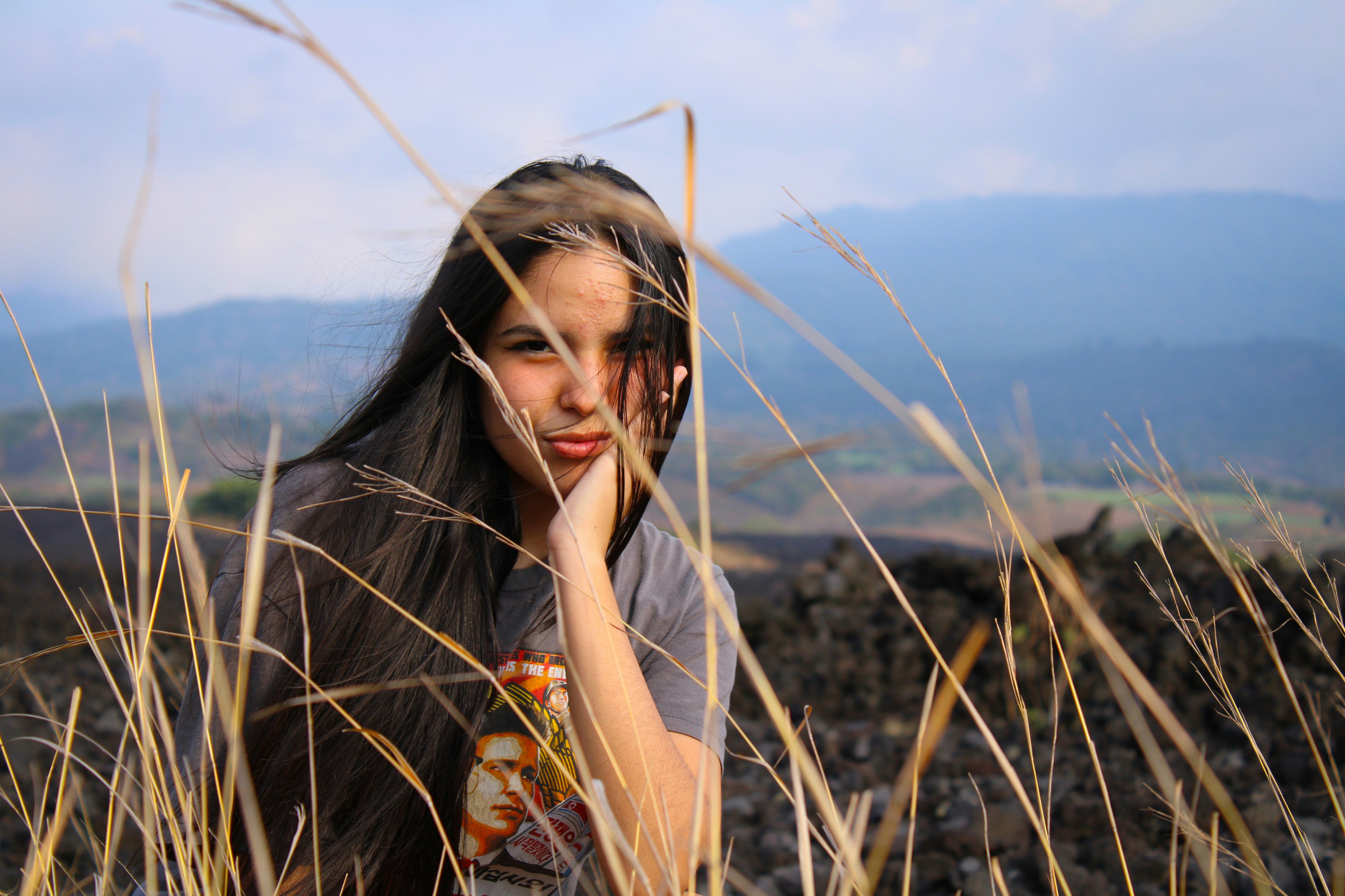 Woman in orange and white floral dress standing on brown grass field during daytime