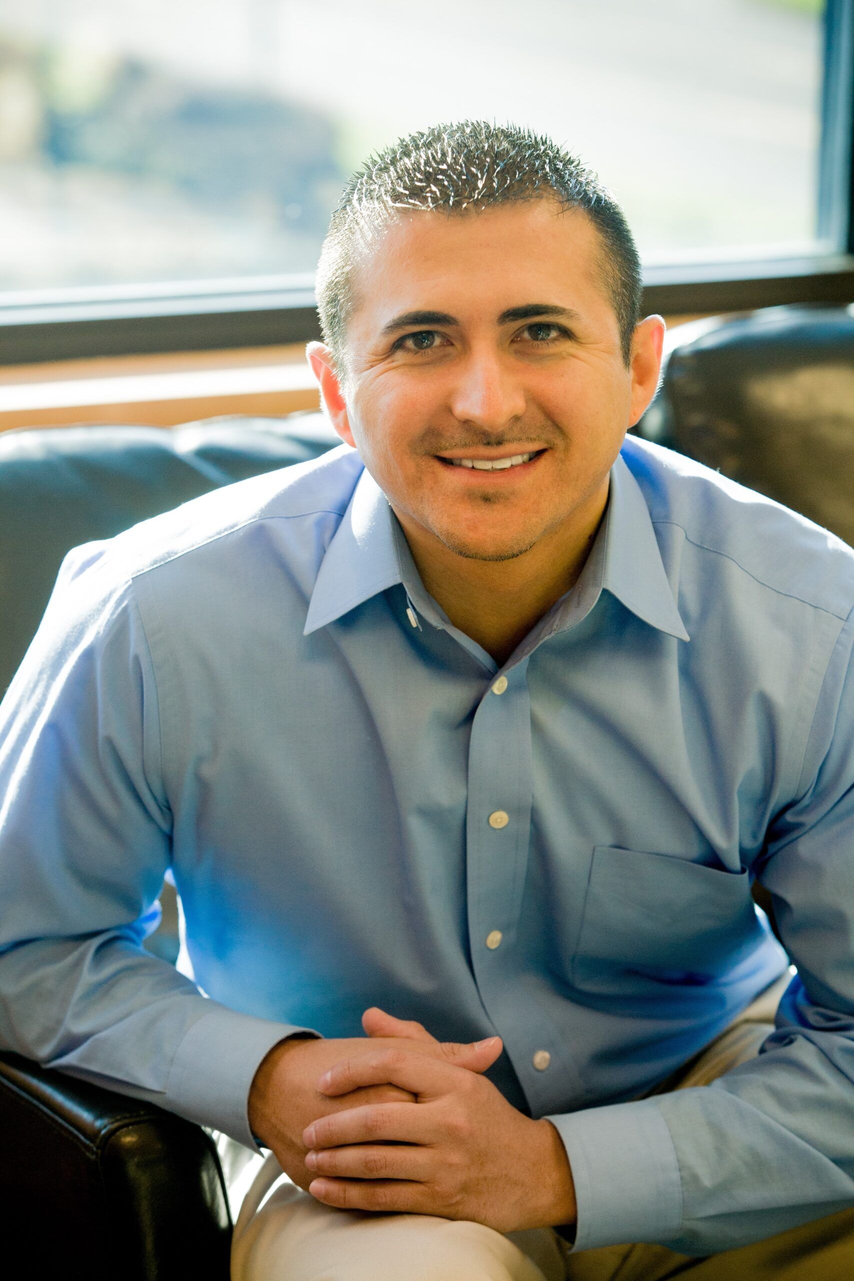 Michael Vallejo, a child therapist, smiling with his hands folded on the arm of the couch in his therapy office.