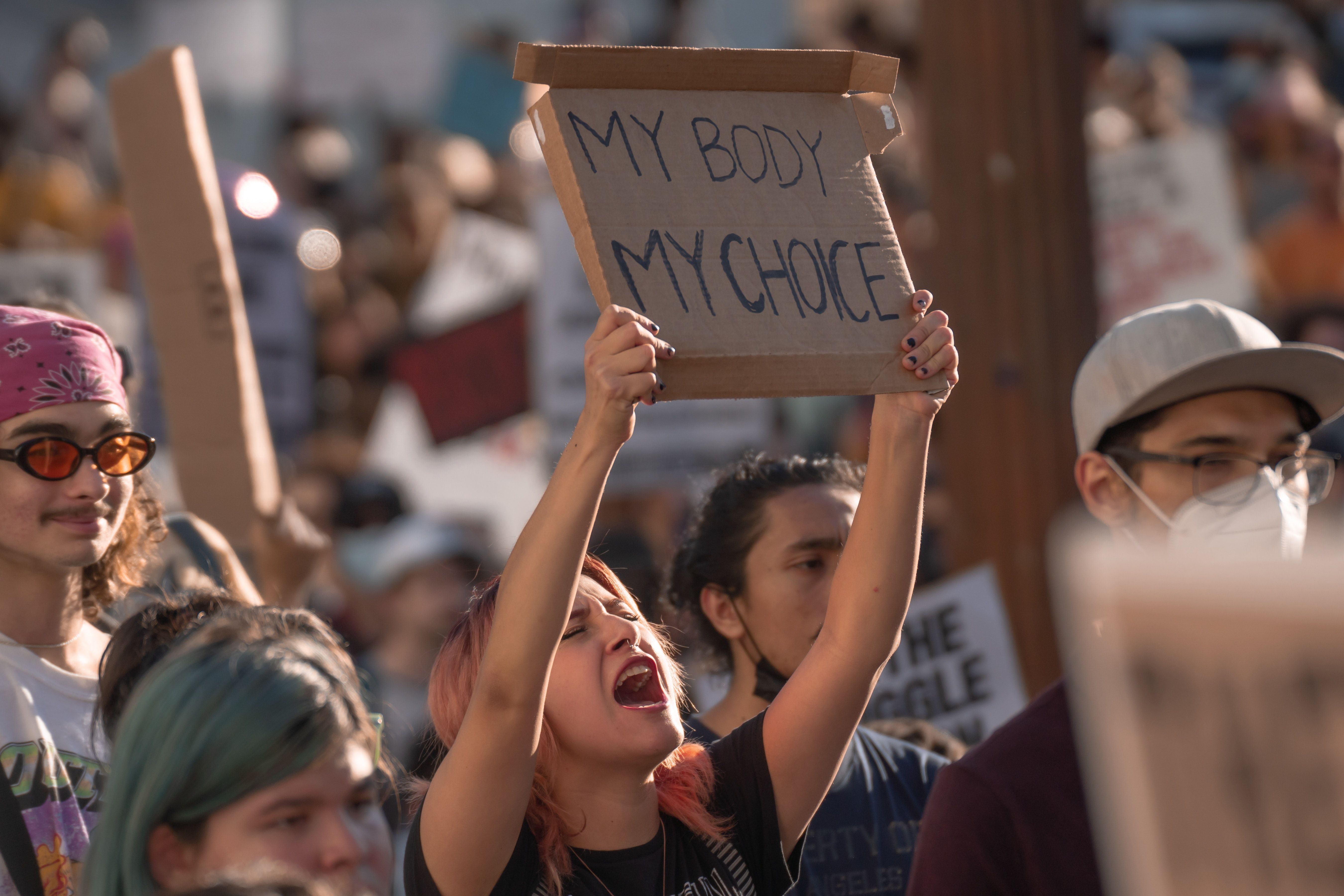 An LA woman protests the US Supreme Court's reversal of Roe v Wade, chanting while holding a cardboard sign that says "My Body My Choice."