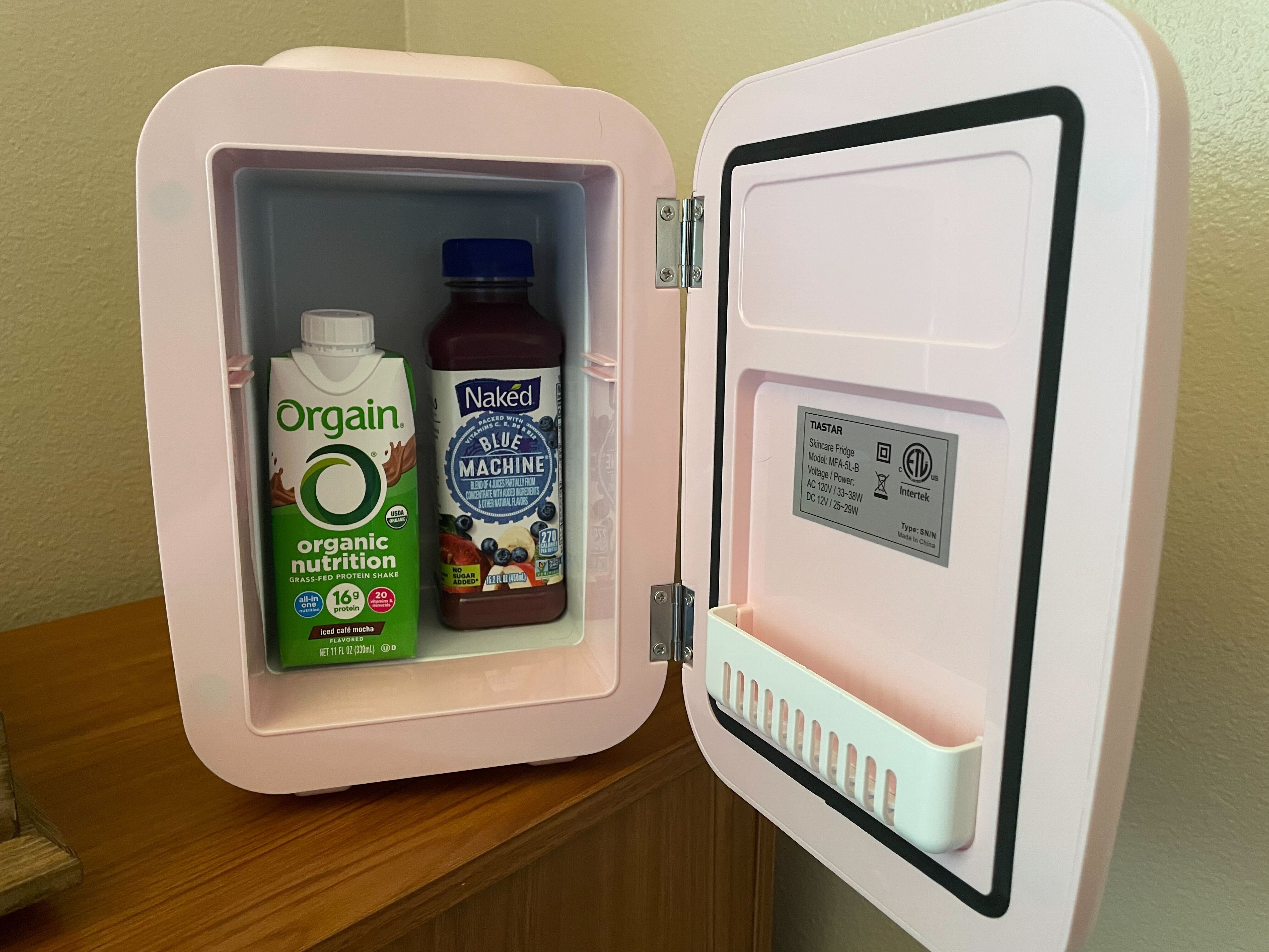 A pink mini-fridge with the door open, revealing an Orgain nutritional shake and a juice smoothie.