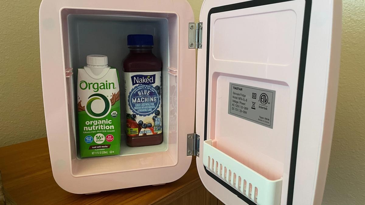 A pink mini-fridge with the door open, revealing an Orgain nutritional shake and a juice smoothie.