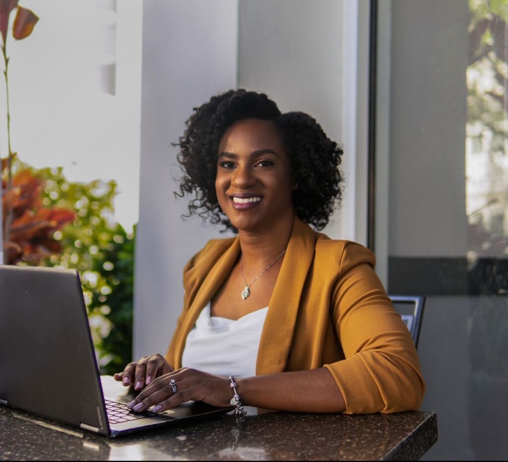 Dr. Shaenor sits at a table, hands poised above the keyboard of a laptop, smiling to camera.