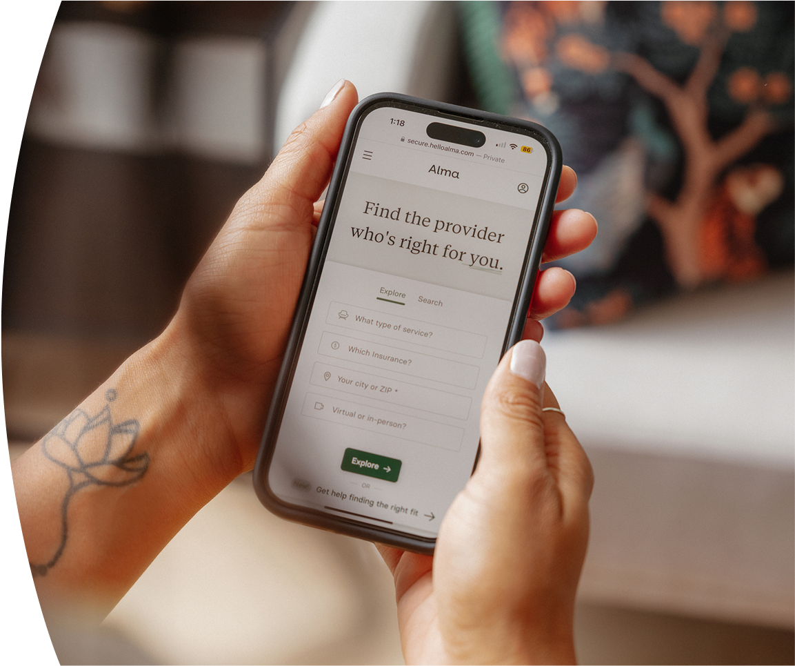 Person holding a smartphone with the Alma website open, showing a provider search tool to find the right therapist based on service, insurance, and location.