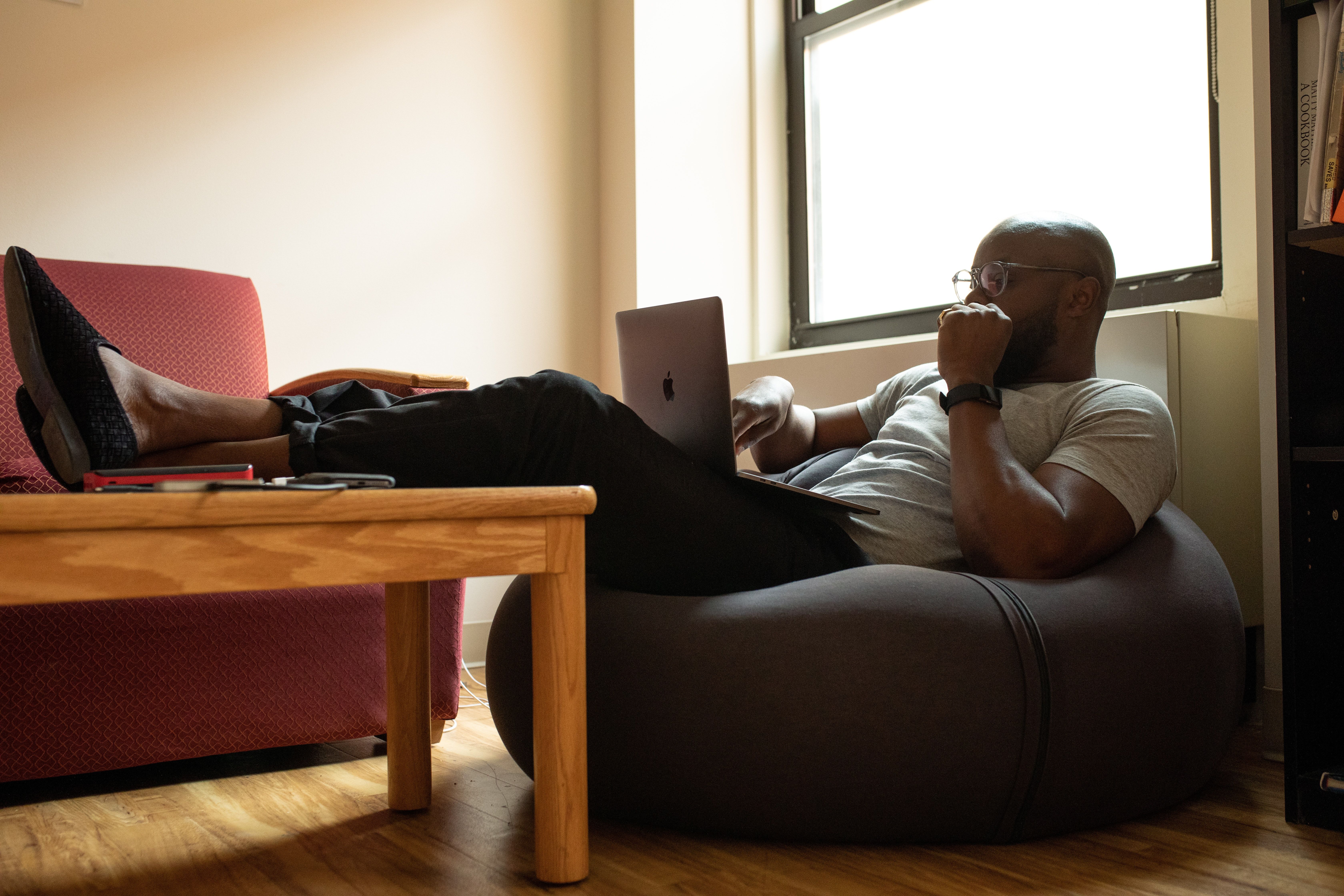 Person sitting in a bean bag chair with legs resting on a table while looking contemplatively at a laptop