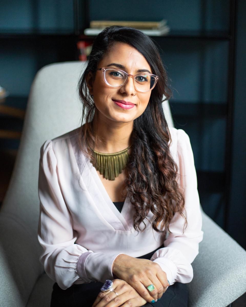 Nira Shah calmly sits in an Alma therapy space with her hands folded over her lap.