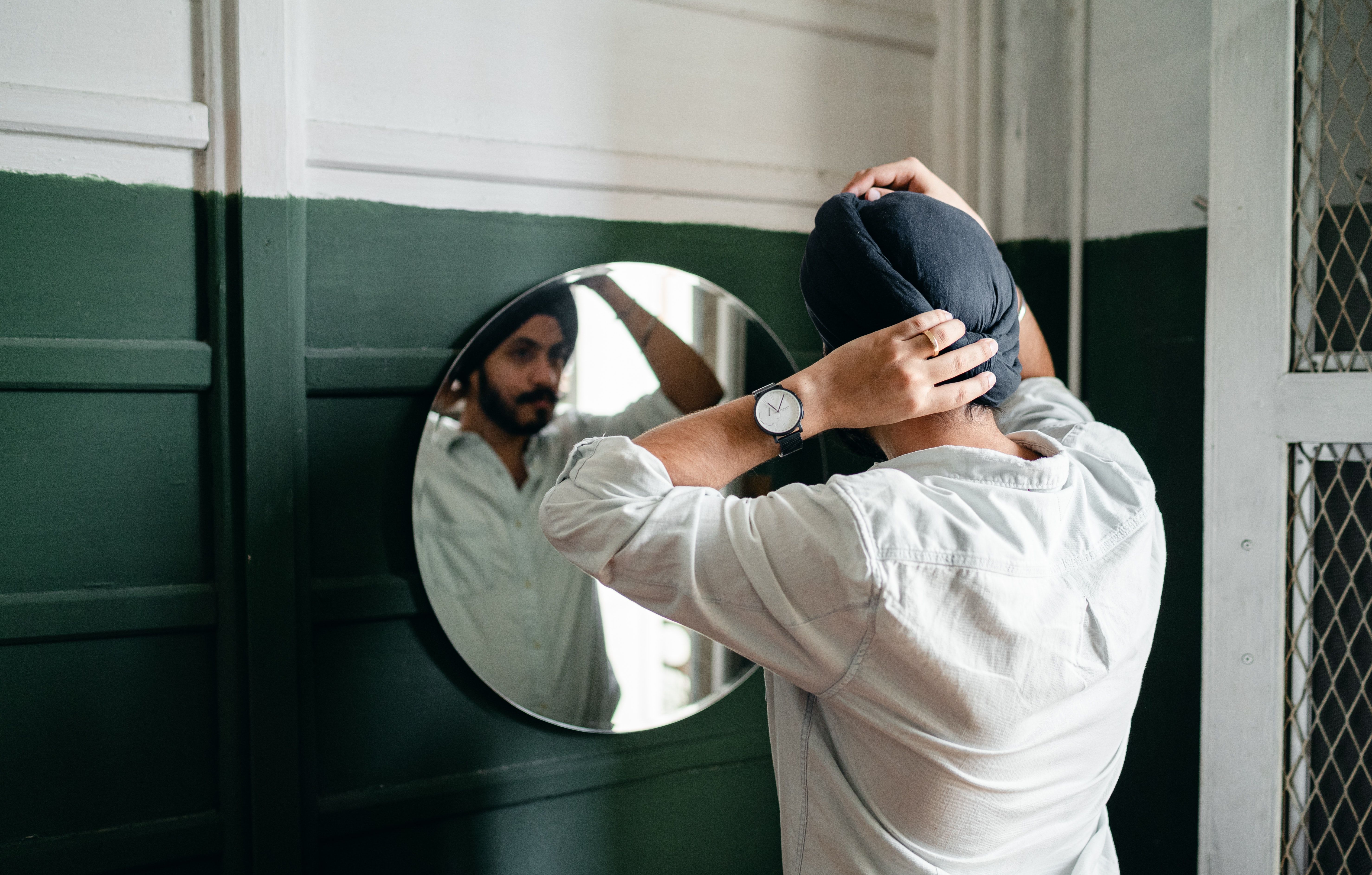 A Sikh man wearing a dastar straightens his turban in the mirror.