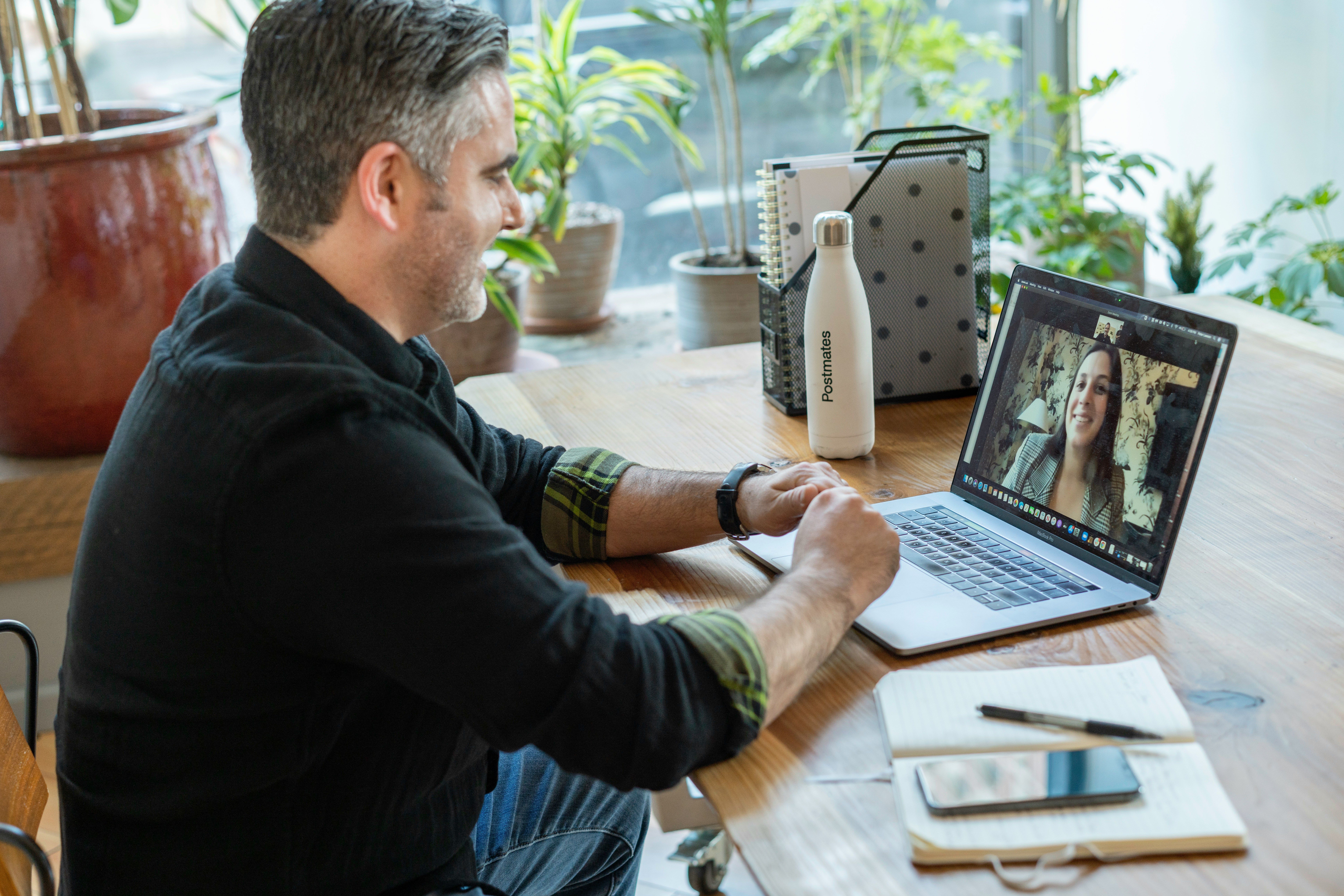 Man in black sweater using a laptop to video conference a female therapist.