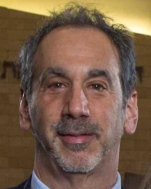 A cropped photo showing a neutral Dr. Mark Serper, gazing to the camera, wearing a suite.