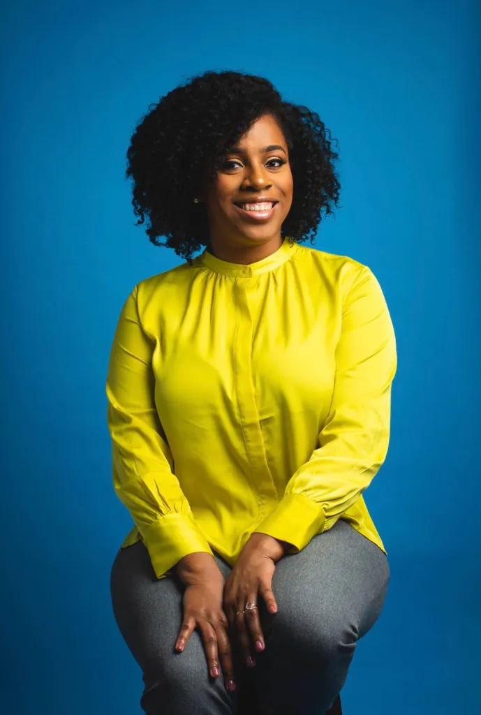 A portrait of Gorgeous West, APC, smiling against a blue studio backdrop.