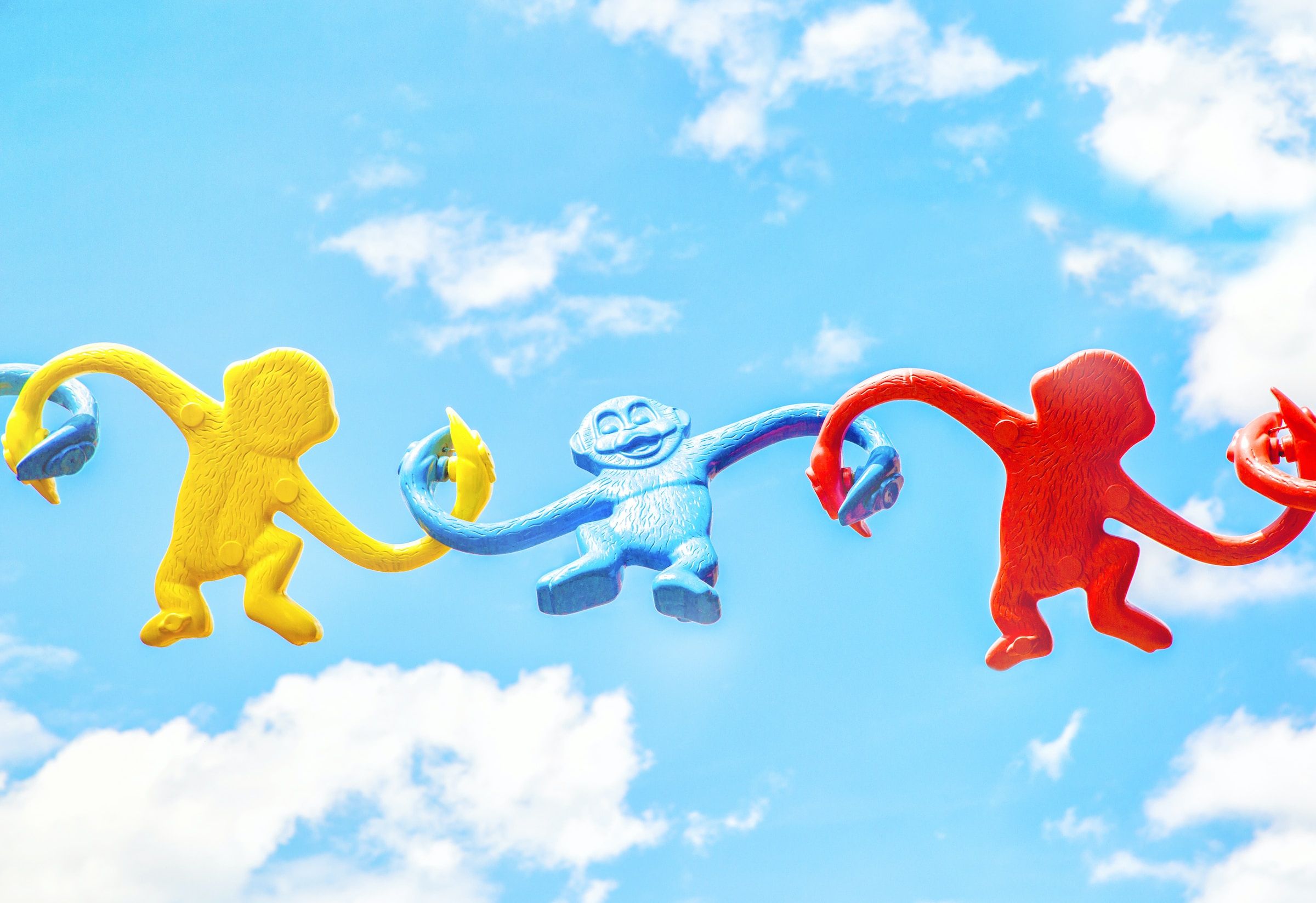 Three different monkey-in-a-barrel figurines, tenuously linked up against the backdrop of a sunny sky, showing the importance of community and a three-pronged approach to fighting stigma.